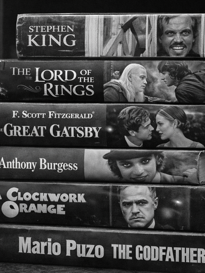 Pila di Libri: Un'immagine ravvicinata dei dorsi di celebri romanzi che hanno avuto famosi adattamenti cinematografici. Si leggono titoli come: The Shining (Stephen King) The Lord of the Rings (J.R.R. Tolkien) The Great Gatsby (F. Scott Fitzgerald) A Clockwork Orange (Anthony Burgess) The Godfather (Mario Puzo)